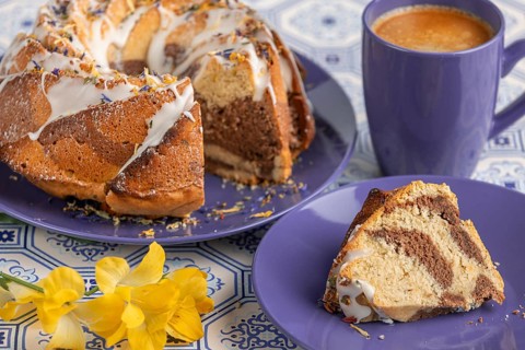 Cut marble bundt cake, cake on blue plates with icing, next to a blue cup of coffee