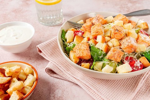 Caesar salad with salmon, with croutons and dressing, in a salad bowl, on a pink table