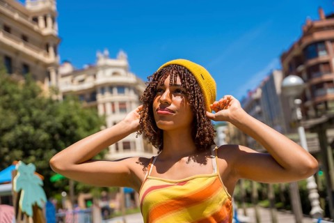 Young woman adjusting her yellow beanie in valencia city center, enjoying a sunny summer day