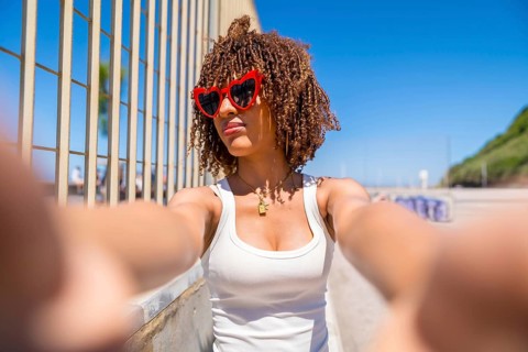 Portrait of a young woman with curly hair taking a selfie wearing heart shaped sunglasses by the