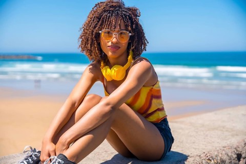 Fashionable young woman enjoying the summer sun and music on a beach wall, embracing the carefree