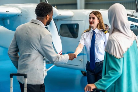 Female pilot shaking hands with businessman next to a private airplane inside an hangar, a