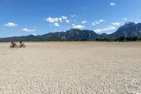 Cracked, dried out ground, waterless Forggensee in spring, behind it Tegelberg massif and Säuling,