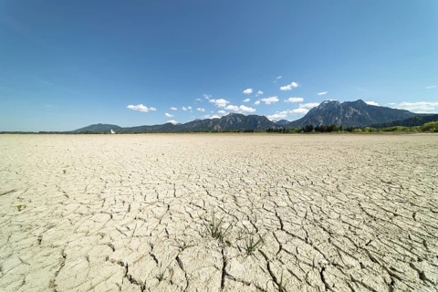 Cracked, dried out ground, waterless Forggensee in spring, behind it Tegelberg massif and Säuling,