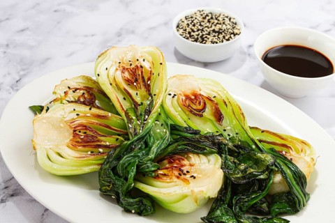 Grilled bok choy served with soy sauce and sesame seeds, on a white plate, homemade, no people