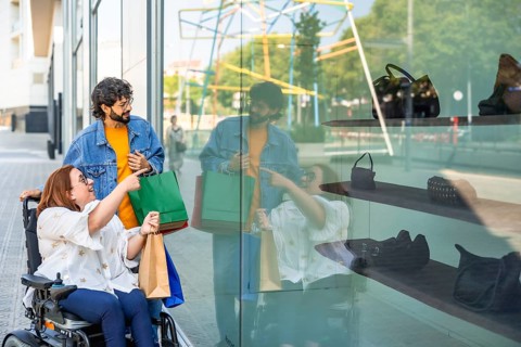 Happy friends doing shopping and looking at a shop window, a disabled woman on a wheelchair is