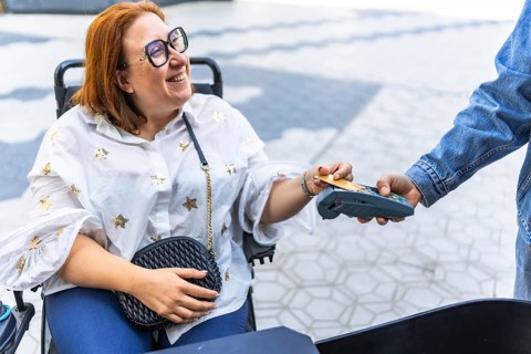 Happy woman using a credit card on a pos terminal while sitting in her wheelchair, enjoying a