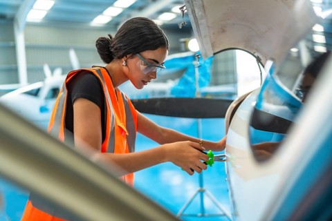 Technician in a hangar performing maintenance on an aircraft engine, wearing safety gear and using
