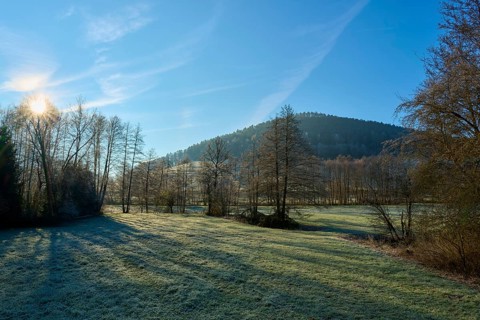 The sky illuminates a meadow and trees in front of a wooded hill, Kirchzell, Amorbach, Odenwald,