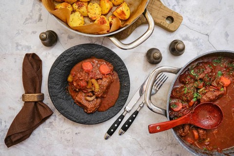 Tender beef stew filled with vegetables is plated on a dark dish, accompanied by a side of seasoned