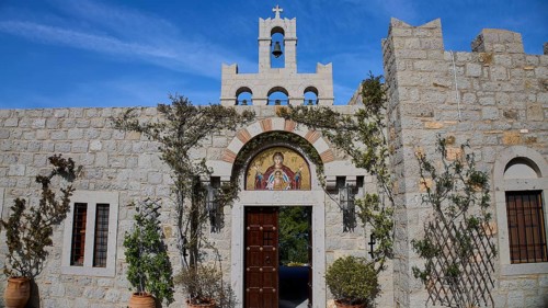 Stone building with bell tower and religious mosaic, surrounded by climbing plants, woman's