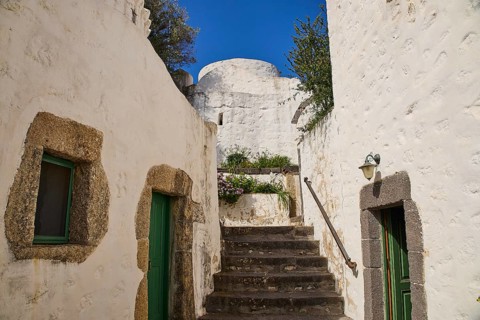 Whitewashed buildings with stone details and green doors under a clear blue sky, Monastery of the