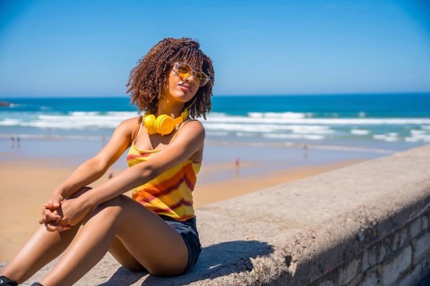Young woman soaking up the summer sun and ocean breeze, enjoying music through her headphones while