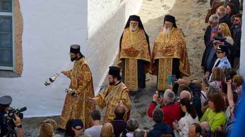 Priests in costly vestments lead a procession through a crowd as people watch and take photos,