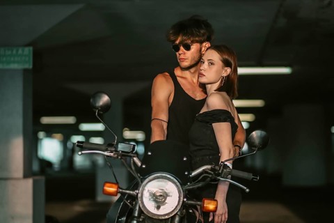A couple in stylish outfits embraces near a motorcycle in a garage