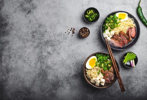 Two bowls of tasty Asian noodle soup ramen with broth, tofu, pork, egg on grey rustic concrete