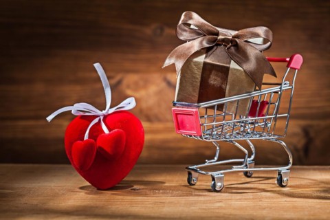 Gift box in shopping trolley and Valentine's heart toy on vintage wood