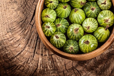 Ripe gooseberries in round bowl on vintage wooden background
