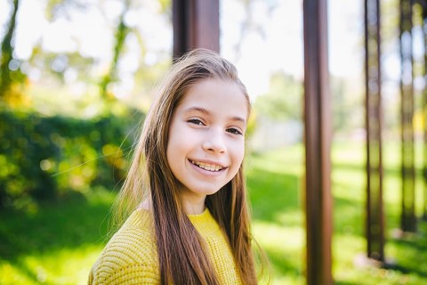 Beautiful teenage girl wearing braces smiling cheerfully dressed in bright yellow clothes outdoors.