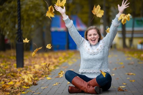 Beautiful girl in the autumn park scatters yellow leaves