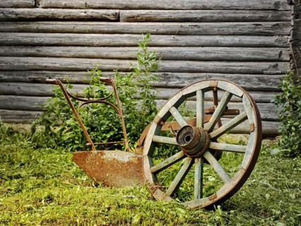Wheel and plough on the grass near the wooden wall