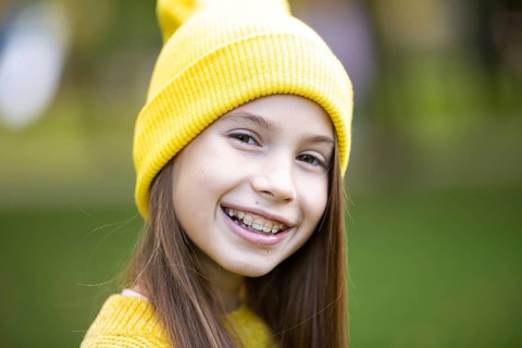 Beautiful teenage girl wearing braces smiling happily dressed in bright yellow clothes outdoors.