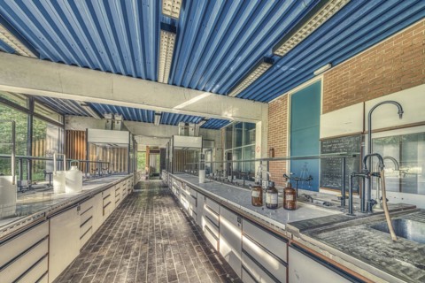 An abandoned laboratory room with long benches and glass containers under daylight, Institute of