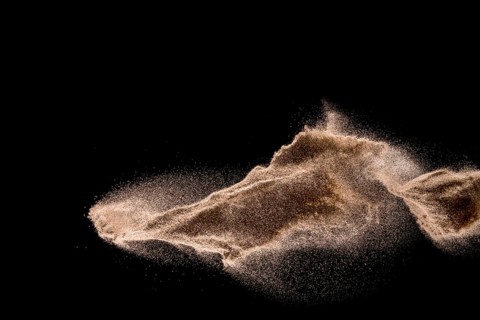 Dry river sand explosion. Golden colored sand splash against dark background