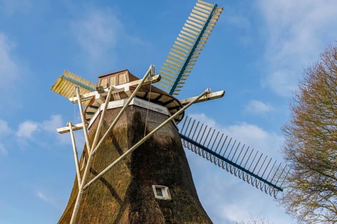 An old windmill with large wings stands under a clear blue sky, burlage, east frisia, germany