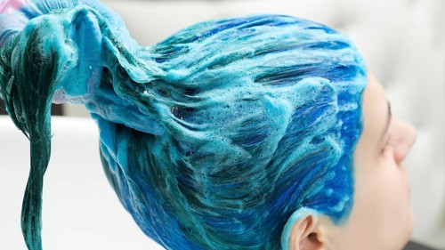 Professional hairdresser holds client's long blue hair in hand while washing hair after process of