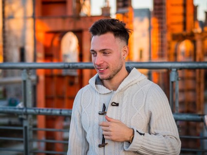 Handsome trendy young man, smiling, standing on a sidewalk in city setting at sunset wearing a