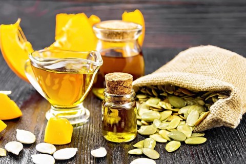 Pumpkin oil in vial, gravy boat and a jar, seeds in a bag and on table, slices of vegetable on