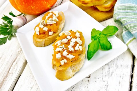 Bruschetta with pumpkin, salted feta cheese in a plate, garlic, basil and parsley, towel and orange