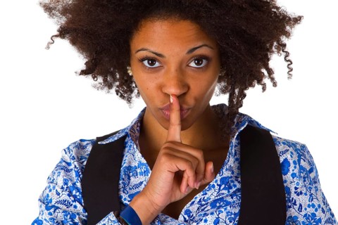 Young African American woman holding index finger in front of mouth - cropped on white background