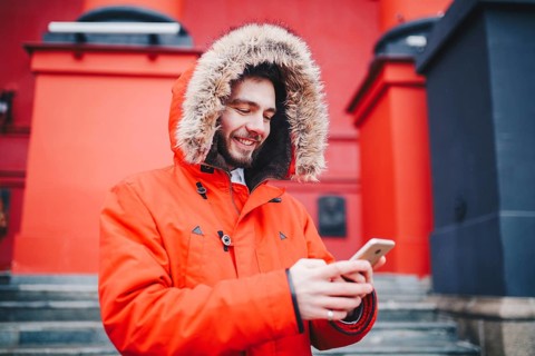 Handsome young male student with toothy smile and beard stands on red wall background, facade of