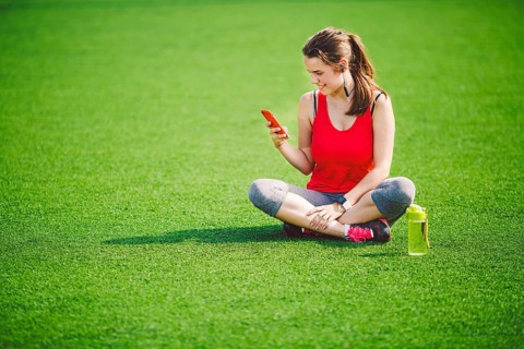 Theme sport health. beautiful young girl sitting resting on green grass lawn stadium using