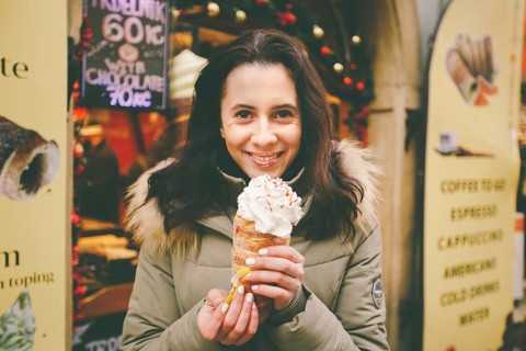 A beautiful girl in a warm jacket eats trdelnik or Trdlo with cream in her hands, in the winter in