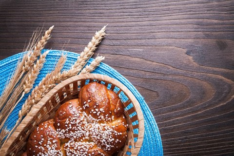 Sweet roll in wicker basket wheat rye ears with wattled table-cloth on wooden vintage board food