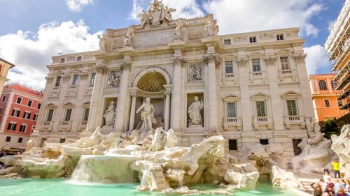 Tourists and people walking next to the Trevi Fountain in a sunny day with clouds, one of the most