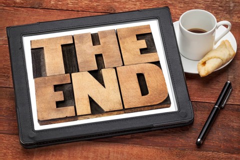 The end - text in vintage letterpress wood type on a digital tablet with a cup of coffee
