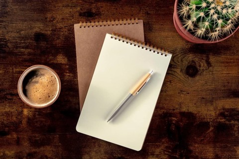 Notebook with a pen, coffee, and plant, overhead flat lay shot on a rustic wooden desk, a mockup,