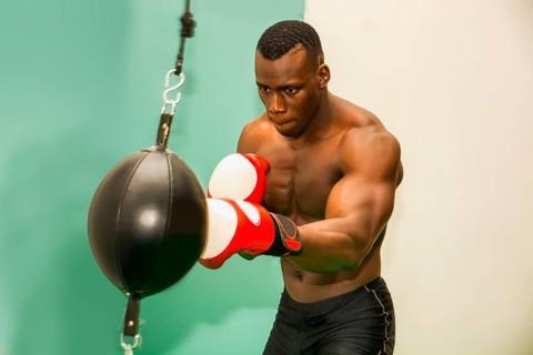 African male boxer punching ball wearing boxing gloves, back profile view
