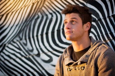 Attractive young man standing against zebra pattern graffiti wall, looking up
