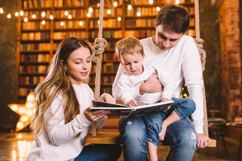 Family togetherness. Mom, dad and son reading story book together sitting on swing evening at home.
