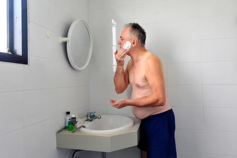 Man 60 plus shaves wet in the bathroom