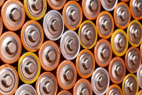 Multiple used AA alkaline batteries are seen arranged in a pile. Closeup side view from the plus