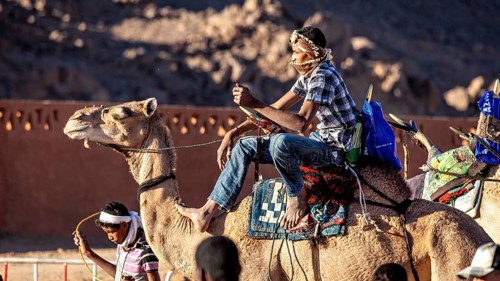 Man riding a camel through the desert, surrounded by mountains, Tuareg camel rider at the