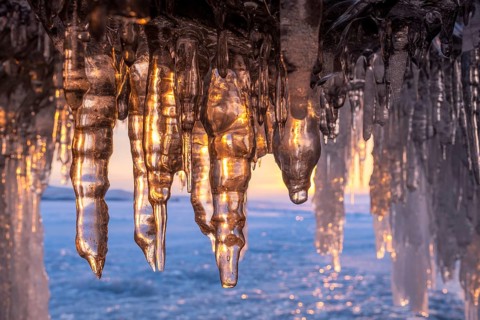 Ice cave on Baikal lake in winter. Blue ice and icicles in grotto in the sunset sunlight. Olkhon