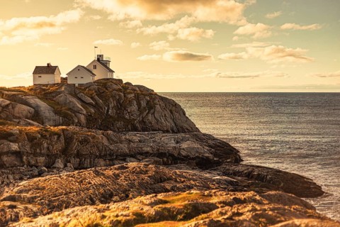 A lighthouse and house on rocky cliffs by the ocean at sunset, creating a serene coastal scene,