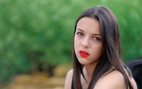 Young beautiful serious brunette girl with red lips and long straight hair over green nature
